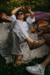 Obraz premium Two short stock sentences: A group of friends lounge on a blanket with sandals and sneakers visible. A casual outdoor picnic scene shows relaxation and easy, sunny vibes.