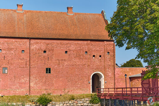 Landskrona, Sweden - 08 August 2025: View of the imposing red brick facade of Landskrona Citadel, its arched entrance framed by a wooden bridge, against a backdrop of green foliage.