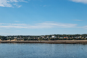 Obraz premium Panoramic view across Saguenay River showing Baie-Sainte-Catherine village shoreline with colorful houses and trees.
