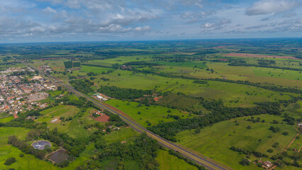 Aerial view of a small town surrounded by lush green fields and a cloudy blue sky © Felippe Lopes