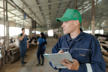 Young caucasian male farmer with cap and clipboard in dairy barn setting