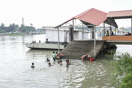 Dhaka, Bangladesh - 11 September 2025: View of children splashing in the river near a pier, with the hazy silhouette of a distant minaret adding to the tranquil scene.