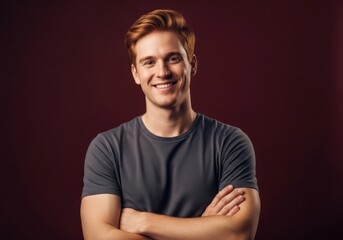 Obraz premium Smiling young man with red hair and crossed arms against a dark red background