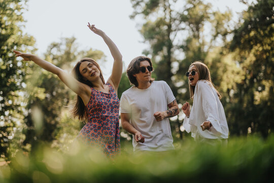 Three young adults dance in a sunny park, smiling and enjoying a carefree outdoor moment.