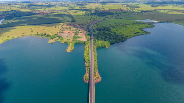An aerial view of a long road bridge spanning a large body of water surrounded by lush greenery and fields