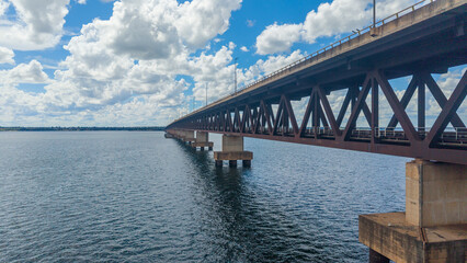 Obraz premium A large steel bridge spans across a body of water under a cloudy blue sky
