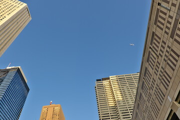 ビル群に囲まれた都会の空を飛行する機体と新宿の午後