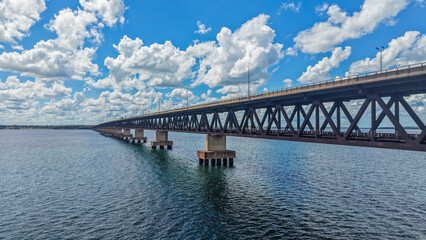 A long bridge stretches across a body of water under a blue sky with fluffy white clouds