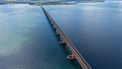 An aerial view of a long bridge stretching across a vast body of water with a small island in the...