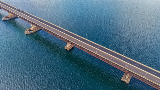 An aerial view of a long bridge spanning across a vast body of water on a sunny day