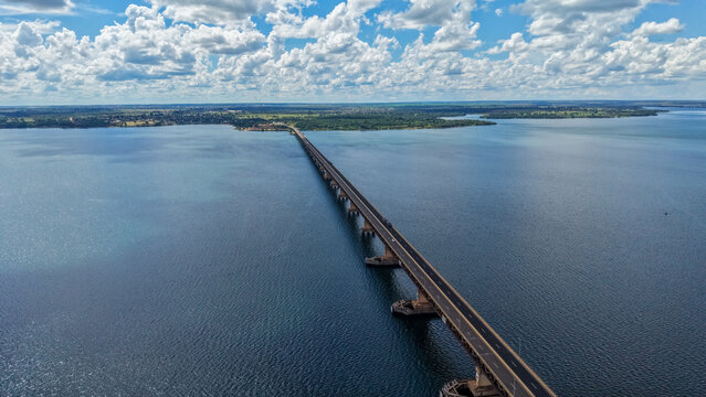 Aerial view of a long bridge extending over a vast body of water under a cloudy sky
