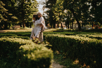 Fototapeta premium Two women share a piggyback moment in a sunny park, smiling and carefree. A playful scene of friends in a green garden for a bright outdoor moment.