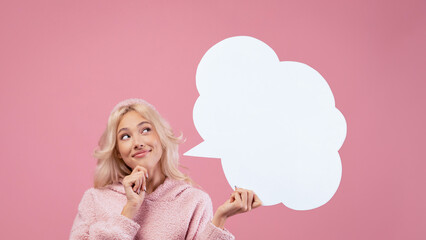 A woman stands in front of a pink background, deep in thought. She holds a blank speech bubble in her hand, pondering her next words. The scene is simple and engaging with bright colors. © Prostock-studio