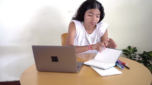 Sleepy and bored teenage girl studying at home with a laptop, yawning and trying to stay awake