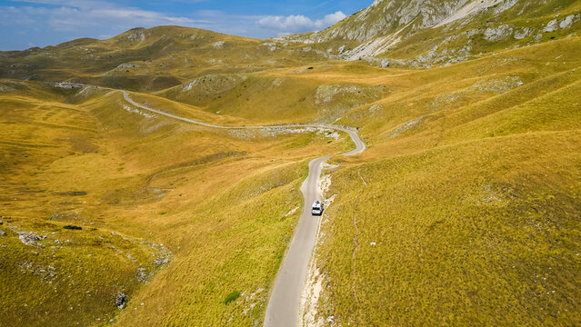 Aerial view of a camper van driving along a winding road at Sedlo Pass in Durmitor, Montenegro, surrounded by rugged mountain landscapes, capturing freedom, adventure, and scenic road travel.