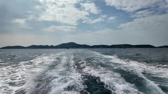 boat departing from lan island, leaving a wake on calm sea with mountainous backdrop
