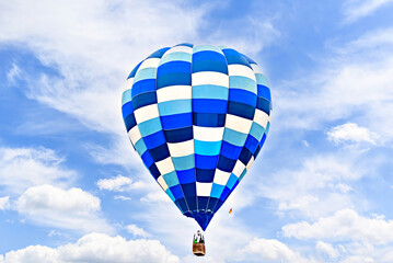 Colorful hot air balloon flying over blue sky with white clouds