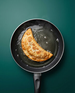 Delicious golden-brown cheburek pastry sizzling and frying in hot oil in a black pan