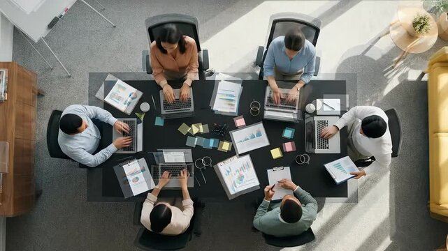Top-down timelapse of diverse business team meeting in modern office, reviewing financial reports, charts and project mind map during strategic corporate planning session.