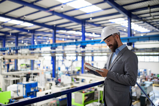 Senior industrial manager reviewing production data on tablet in modern factory.