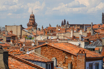 Overlooking the charming rooftops of Toulouse, the warm terracotta tiles contrast with the clear blue sky, highlighting the city's historic buildings and vibrant atmosphere in summer