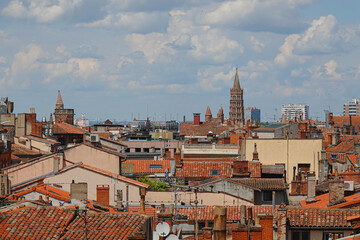 Obraz premium Rooftops of Toulouse showcase a blend of historic and modern architecture under a vibrant sky. The iconic tower and terracotta tiles create a picturesque view of the city