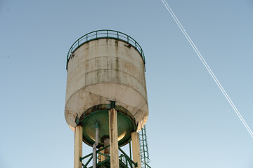 A water tower illuminated by the rays of the evening sun. A tall water tower against a blue sky.