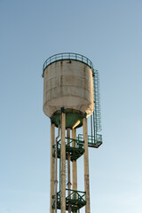 A water tower illuminated by the rays of the evening sun. A tall water tower against a blue sky.