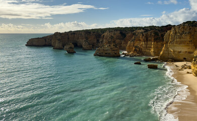 Sandy beach with rocky cliffs, vegetation and blue cloudy sky © Angelov