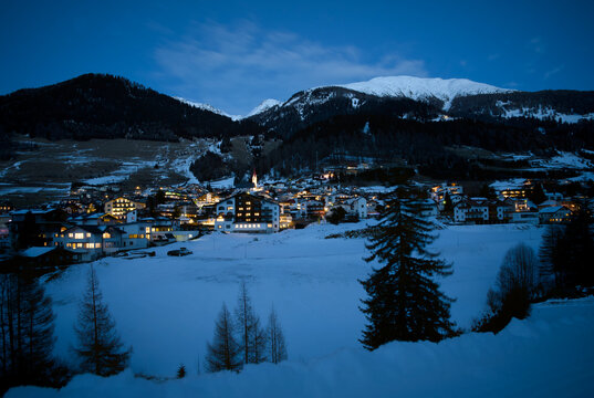Nauders Village at Winter Evening, Tyrol Austria: Illuminated Houses, Snowy Alps Background