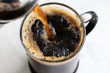 Hot coffee pouring into glass mug with foam on white marble surface
