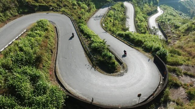 An aerial view of a winding road in Doc Tham Ma Pass, Dong Van, Ha Giang, Vietnam, shows the challenging terrain and lush vegetation.