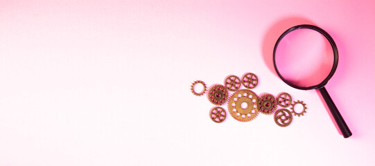 Magnifying glass and gears on a pink background. Business concept.