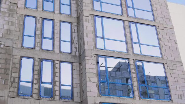 Building Facade Windows Installation. Facing Building Construction Site. Monolithic Concrete Frame of Apartment Building, Construction with Ready-Made Facade Aerated Concrete Blocks