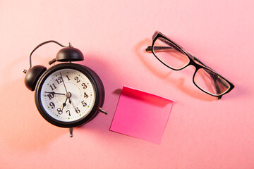 Retro alarm clock and eyeglasses on pink background. Time management concept