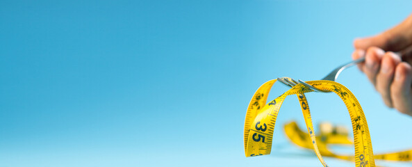 Closeup of a fork with a yellow measuring tape on a blue background