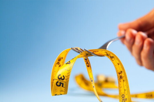 Closeup of a fork with a yellow measuring tape on a blue background