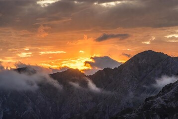 Radiant sunset paints the mountain peaks with golden hues and shrouds them in mystical mist