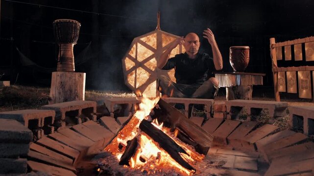 Man Conducting a Campfire to Ethnic Music at Night, Surrounded by Traditional Instruments