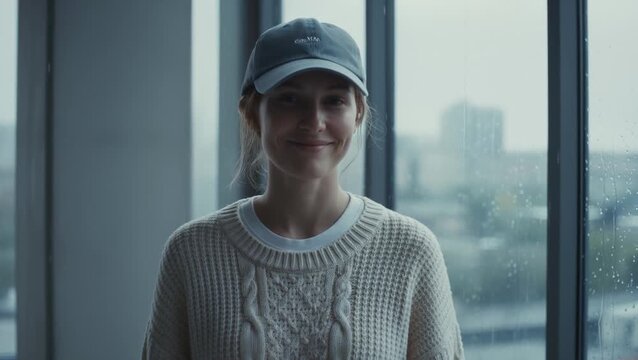 Woman Wearing Baseball Cap and Sweater Smiling at the Camera on a Rainy Day