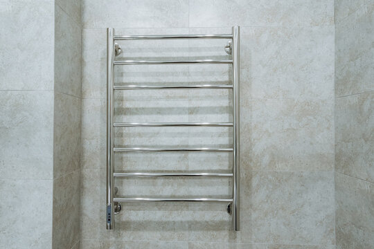 Elegant Chrome Radiator On Wall. Minimalist Gray Tiles With Mounted Towel Rack. Contemporary Apartment Feature Showcasing Stylish Heated Towel Rail With Mounting Brackets And Grout