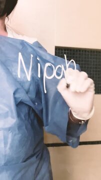 Women caucasian unrecognisable  doctor writing zoonotic Nipah virus on glass board in hospital lock down camera