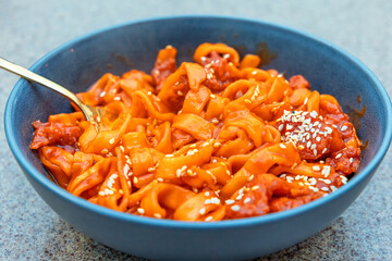 Close up view of tasty Asian noodles tossed in spicy sauce and garnished with sesame seeds in a dark bowl