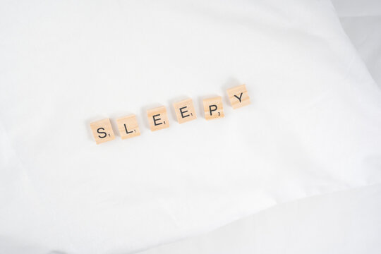 Naestved, Denmark, December 14th, 2025. Scrapple wooden letter tile spelling "Sleepy" on white hotel bedding.