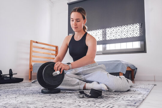 Home workout, young woman setting up barbell for strength training, indoor home gym routine, fitness equipment and wellness lifestyle.