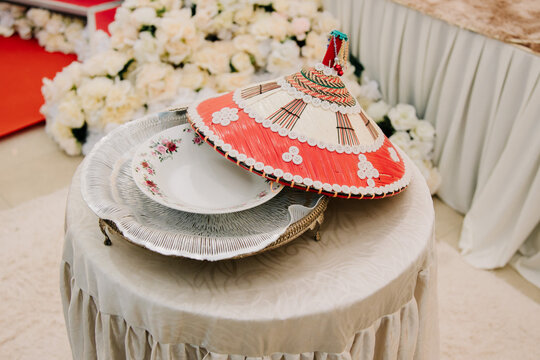 Traditional Malay Wedding Tudung Saji and Plate.A traditional decorative Malay food cover (Tudung Saji) in red and white placed on a ceremonial table with a floral porcelain plate.