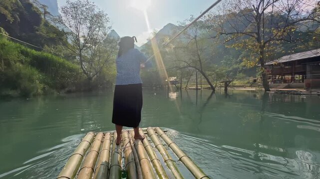 A woman stands on a bamboo raft, navigating the tranquil watersHang Than Lim, Yen Minh, Ha Giang, Vietnam, enjoying the scenic landscape.