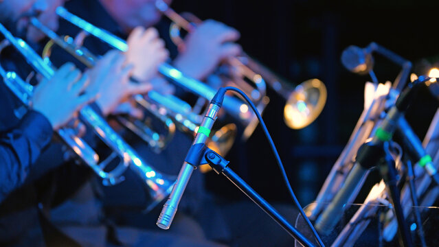 Close-up of a microphone in focus with a blurred orchestra in the background. Blurred orchestra brass section playing trumpets during a live concert