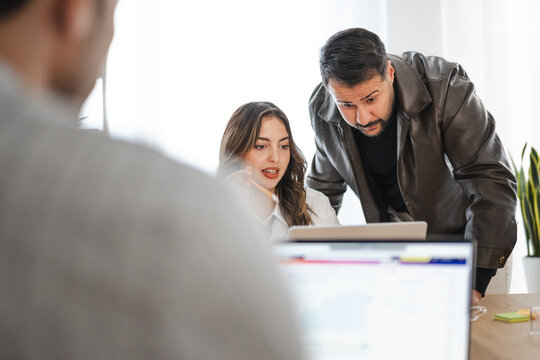 A man and a woman collaborate on a project, reviewing information on a tablet in an office setting.