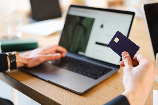 A person's hands are shown as they use a laptop and hold a credit card, suggesting online shopping or a financial transaction.